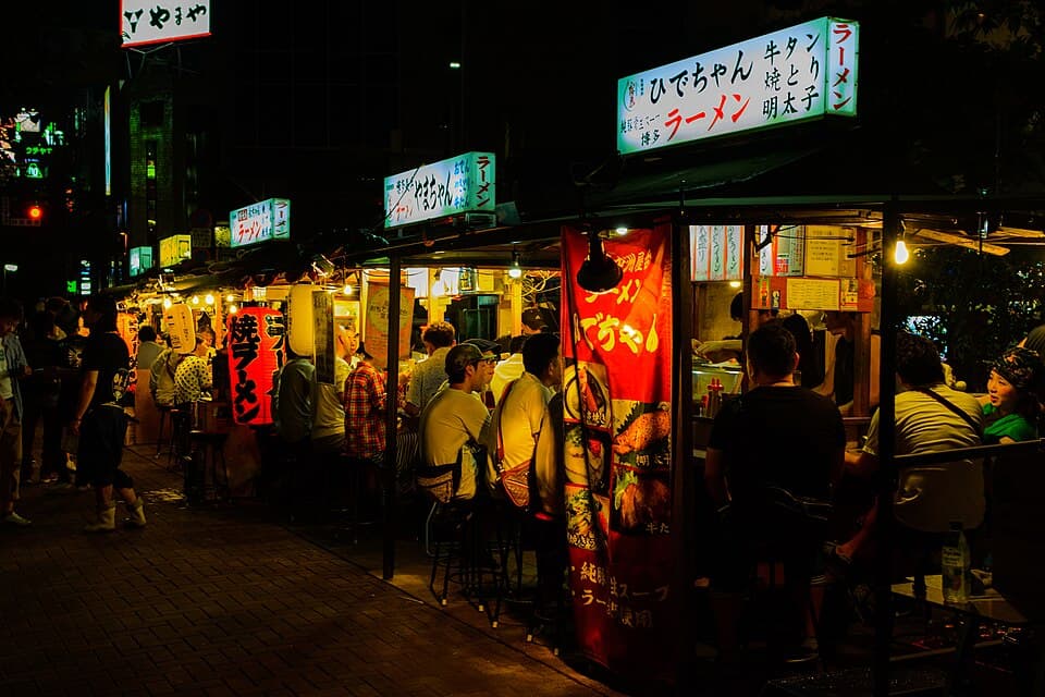 Evening yatai food stalls with diners beside the Naka River in Nakasu, Fukuoka.
